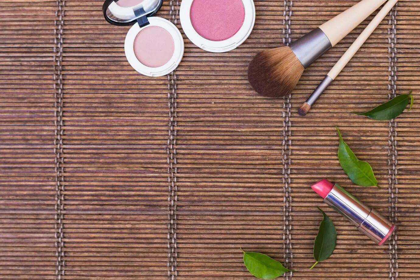 Auf einem Tischset liegen Rouge, ein Lippenstift und Make-up-Pinsel.